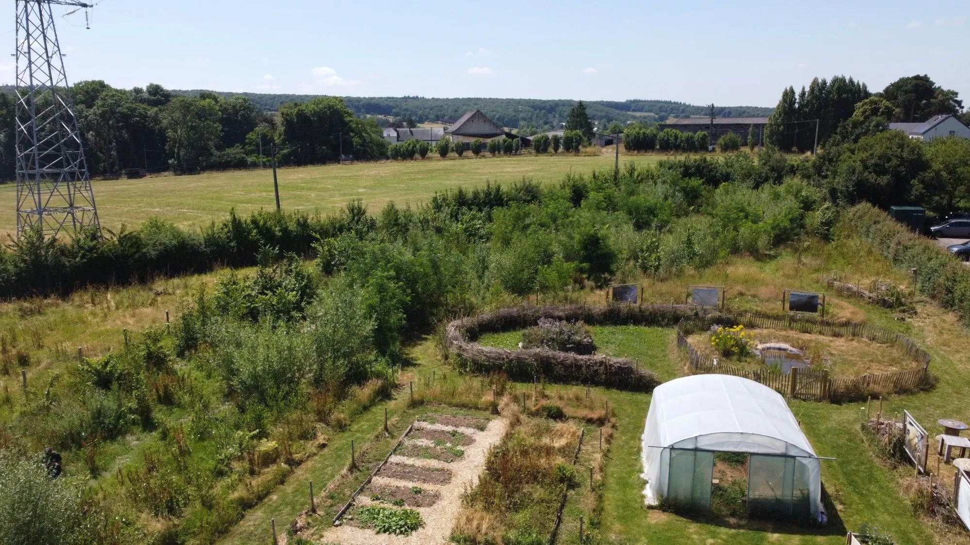 Vue aérienne des Jardins d’ici : le potager, la serre, la mare, les structures en saule et la forêt nourricière